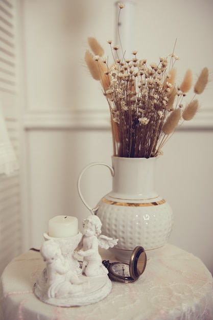 Candeliere con angeli e vaso bianco con fiori secchi sul tavolo