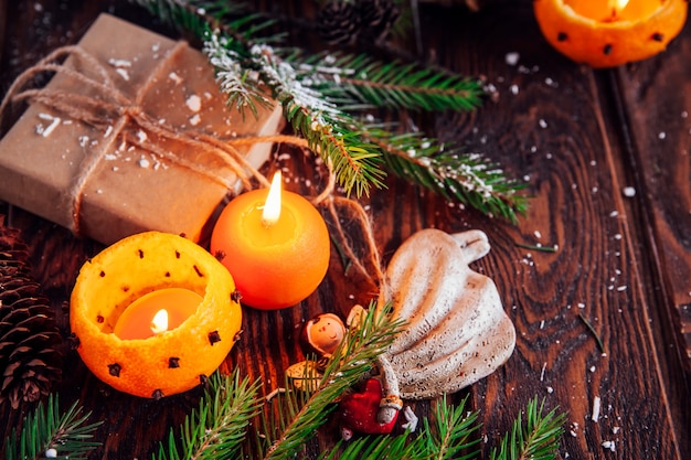 Candlesticks made of mandarins with snowy fir branches, toys and presents on wooden table. Christmas and New Year background.