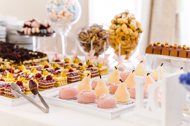 Candy bar. Table with different sweets for party. Dessert table for wedding party. Decorated delicious. Sweets, candies, dessert, cupcakes, tartlets,macaroon, cakes and muffins.