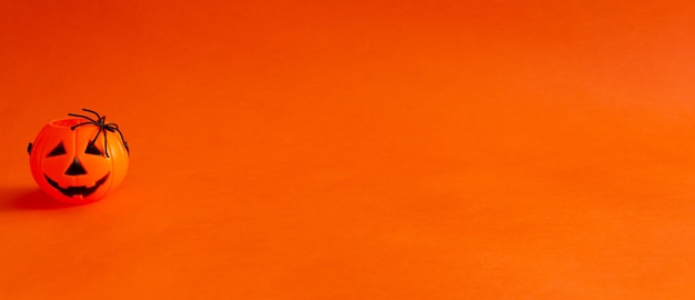 Cestino di caramelle a forma di zucca di lanterna di halloween su sfondo arancione con uno spazio di copia di un ragno