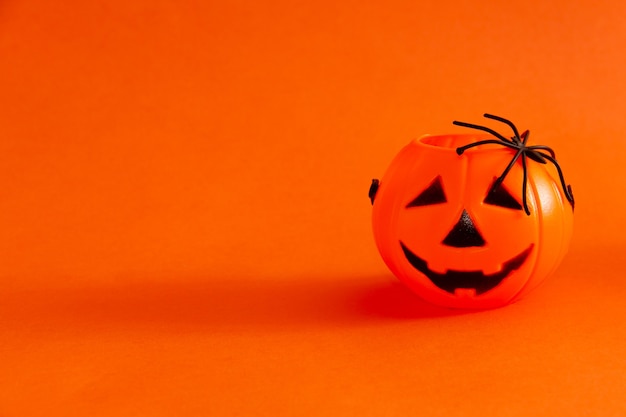 Candy basket in the shape of halloween lantern pumpkin on orange background with a spider Copy space