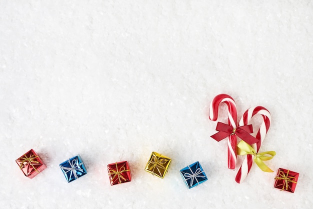 Candy cane decorated with small gifts on white snow background. Copy space