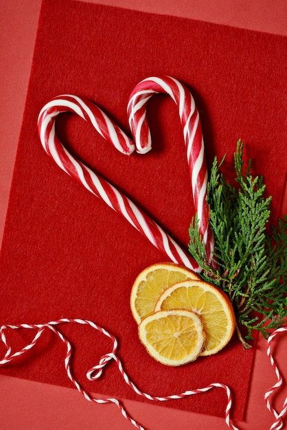 Photo candy cane, dried orange slices  with a sprig of fir on a red background.