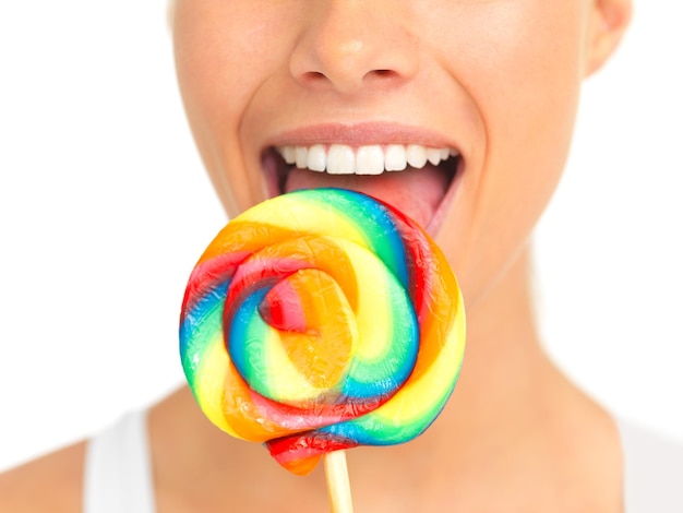 Candy lollipop and sweets with a woman in studio isolated on a white background eating a sweet snack Food bright or color with a young female holding and licking a giant lolly closeup alone