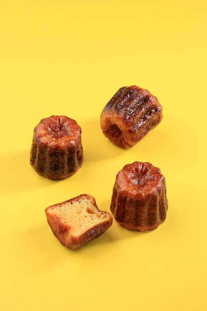 Canele or cannele, french pastry from bordeaux. rum and vanilla
flavors with a tender custard center and a thick caramelized crust.
isolated on yellow background, selective focus