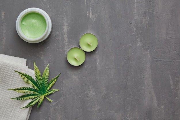 Cannabis hemp cream with marijuana leaf and candles on a gray concrete table with copy-space. cannabis topicals cosmetics concept.