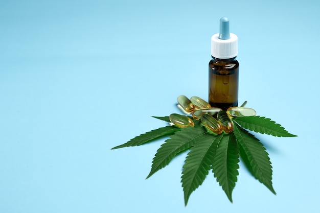 Olio di canapa cannabis cbd in pillole e bottiglia sulla foglia di marijuana verde sul blu