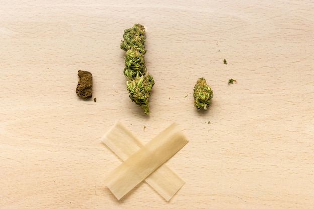 Cannabis in its various forms marijuana and hashish with rolling paper to prepare a joint on a wooden table