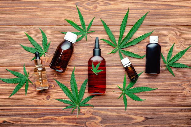 Cannabis medische vloeistoffen en cosmetische producten. Hennep cbd olie en medicijnflessen met marihuanaplant en wietbladeren op bruine houten ondergrond. Medicinale marihuanaplant Cannabis Sativa. Bovenaanzicht.