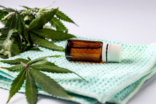 Cannabis oil extract in a glass jar located on a white background with hemp leaves, horizontal orientation, closeup