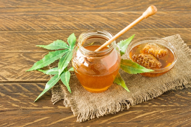 Cannabisbladeren, marihuana en verse biologische pure honing in glazen pot op houten tafel achtergrond. Honing CBD-concept.