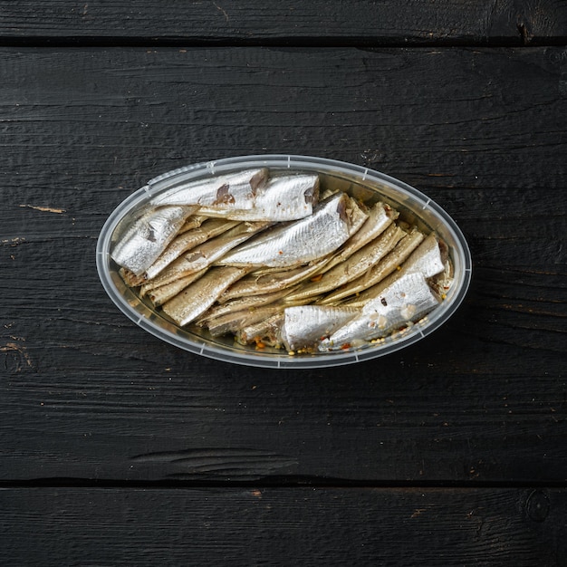 Canned Anchovy  set, in plastic container, on black wooden table background, top view flat lay, square format