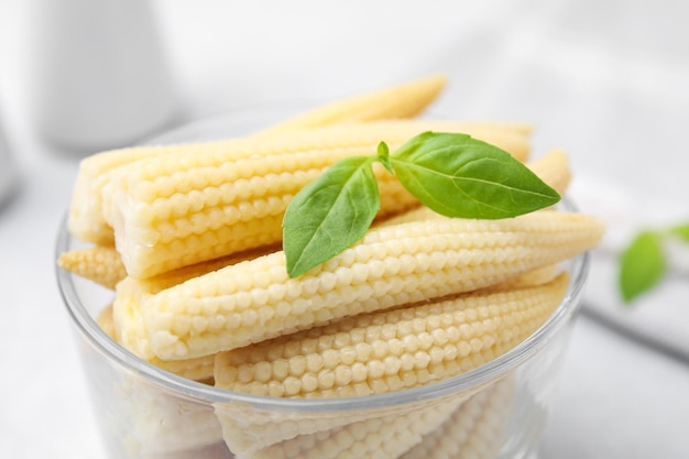 Canned baby corns with basil on white table closeup