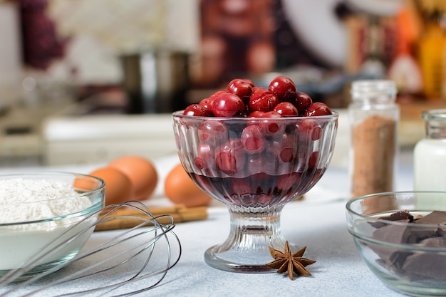 Canned cherries in a glass bowl and the ingredients for making a pie are prepared on the table