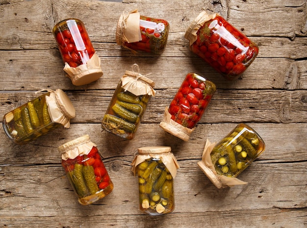 Canned cherry tomatoes and cucumbers in glass jars on a dark background top view