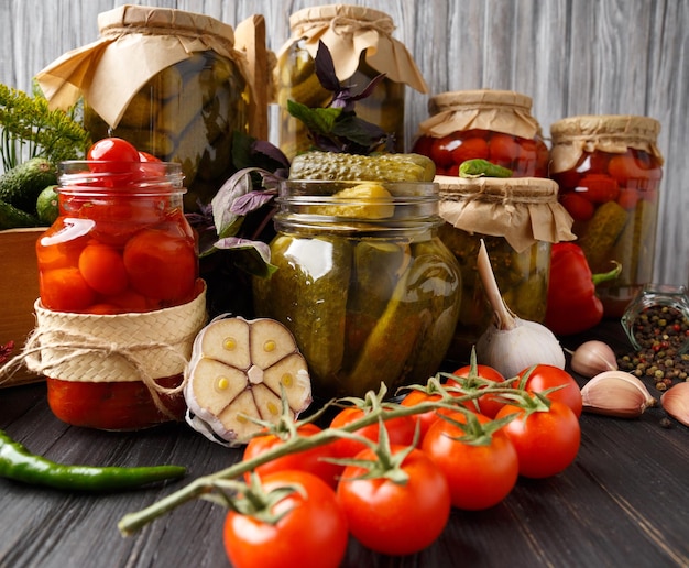 Canned cherry tomatoes and gherkins in jars fresh vegetables spices and herbs for marinade on a wooden background
