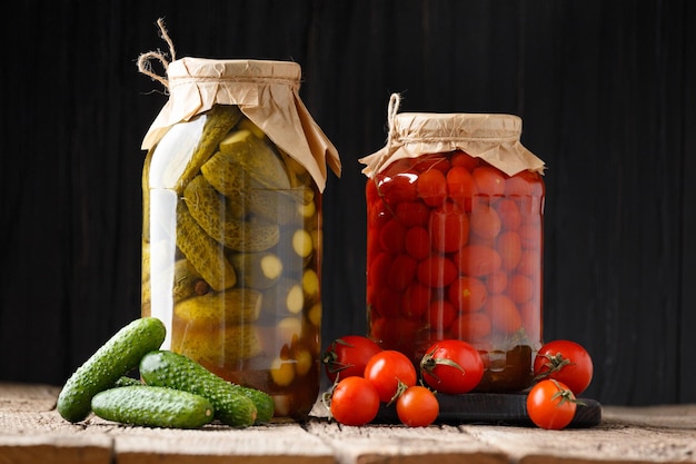 Canned cucumbers gherkins and cherry tomatoes in jars fresh vegetables for preservation on a dark wooden background