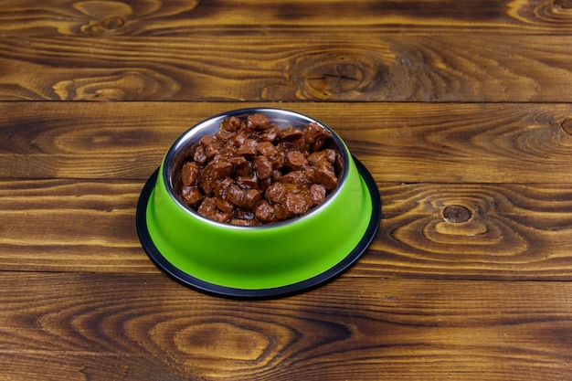 Canned food for cats or dogs in green metal bowl on wooden floor