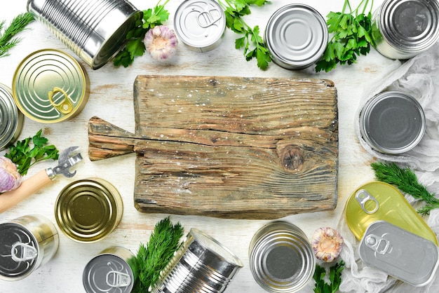 Canned food in tin jars on white wooden background Top view