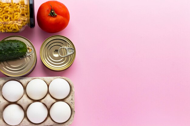 Canned goods, fresh vegetables, tomato and cucumber, chichen\
eggs and pasta in glass jar on pink background