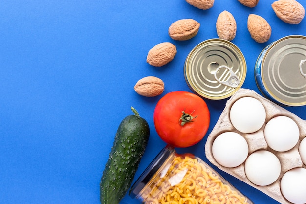 Canned goods, walnuts, fresh vegetables, tomato and cucumber, chichen eggs and pasta in glass jar on blue background