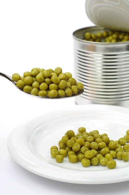 Canned green peas in spoon and plate on white