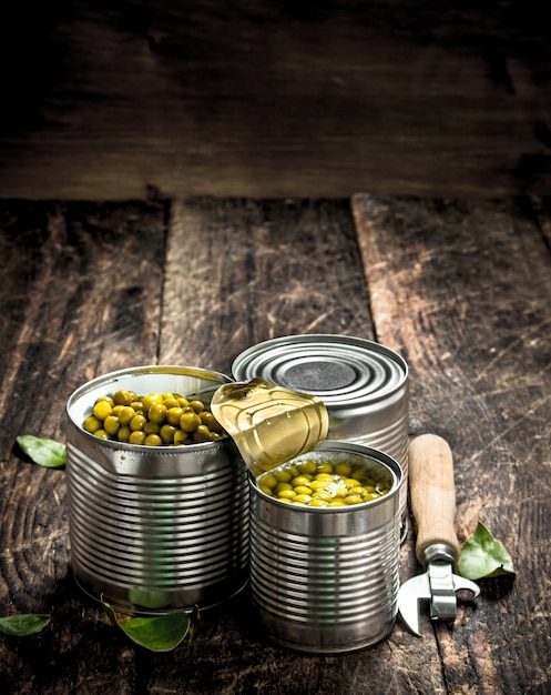 Canned green peas in a tin can with opener on a wooden background