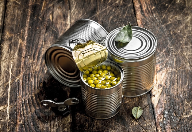 Canned green peas in a tin can with opener. On a wooden background.