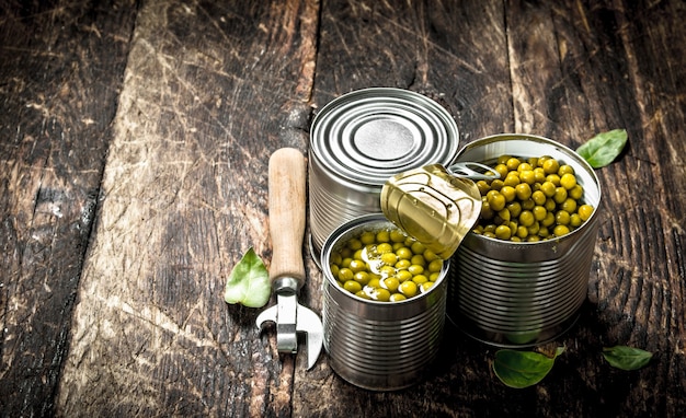 Canned green peas in a tin can with opener. On a wooden background.