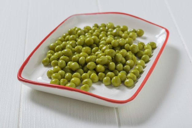 Canned green peas in a white plate with a red border. Dietary vegetarian food.