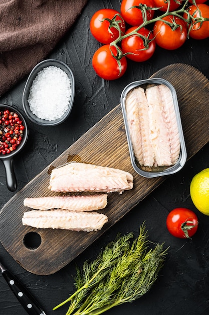 Canned Mackerel Fillets in Tin set, on wooden cutting board, on black background with herbs and ingredients, top view flat lay