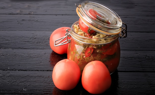 Canned pickled tomatoes in a glass jar on a black wooden table rustic style