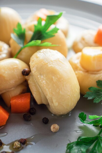 Фото Консервированные белые грибы крупным планом в серой тарелке с морковью и зеленью