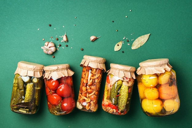 Photo canned and preserved vegetables in glass jars over green background top view flat lay copy space