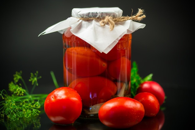 Canned ripe red tomatoes with spices in a large glass jar isolated on a black background
