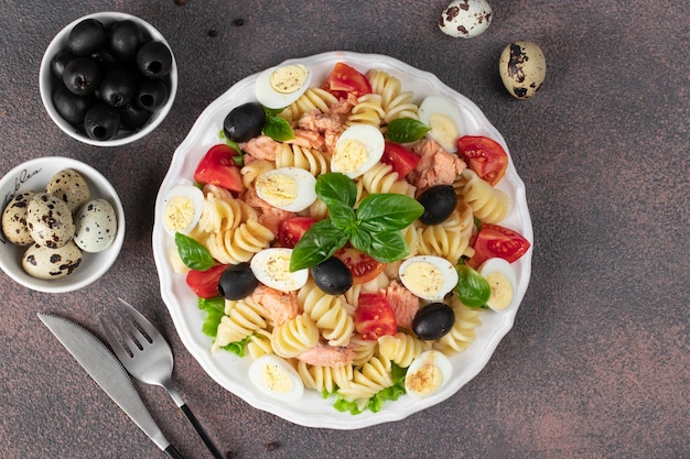 Photo canned salmon salad with pasta cherry tomatoes quail eggs basil and black olives on brown background copy space