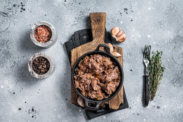 Canned stewed horse and beef meat in a pan. Gray background. Top view.