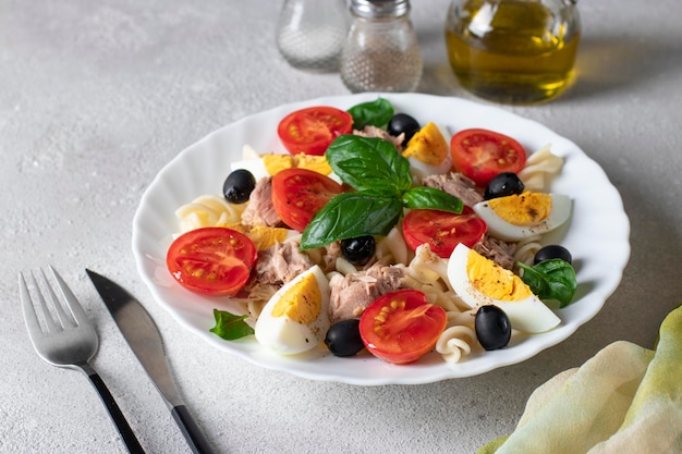 Insalata di tonno in scatola con pasta pomodorini olive nere uova sode e basilico su sfondo grigio cibo sano