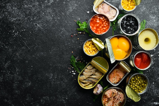 Canned vegetables beans fish and fruits in tin cans on black stone background Food stocks