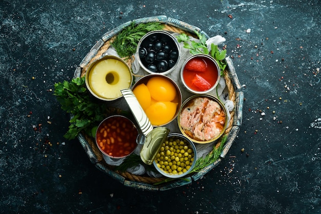 canned vegetables, beans, fish and fruits in tin cans on black stone background. food stocks.