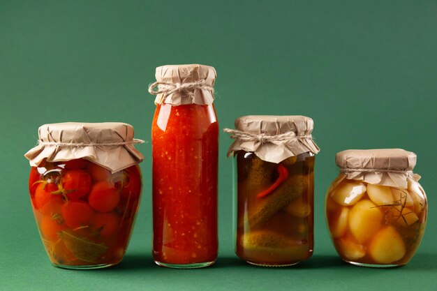 Photo canned vegetables in jars on a green background pickled cucumbers tomatoes garlic chili sauce