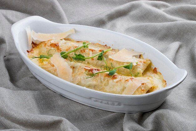 Cannelloni met gehakt gebakken in een witte keramische plaat op textielachtergrond