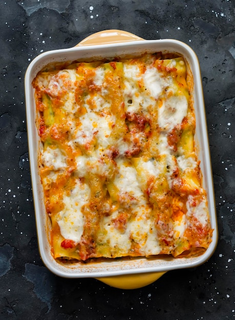 Cannelloni met spinazie en ricotta gebakken met mozzarella in een ovenschaal op een donkere achtergrond bovenaanzicht