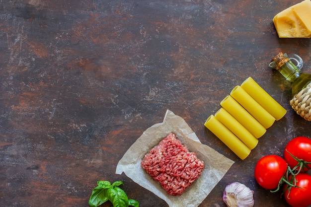 Cannelloni, tomaten, gehakt en andere ingrediënten. Donkere achtergrond. Italiaanse keuken.