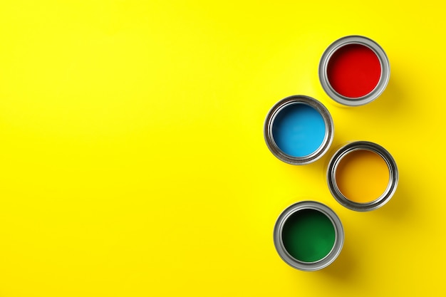 Cans of different paints on yellow background, top view