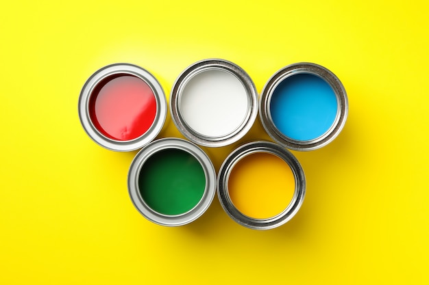 Cans of different paints on yellow surface