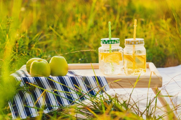 Cans of lemonade on the picnic table. Wildflowers and green apples are nearby