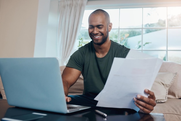 cant be accused of not working hard shot of a young businessman reading paperwork while working on his laptop