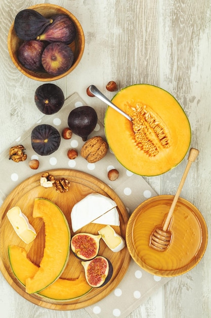 Дыня мускусная дыня, нарезанная прошутто, хамон, листья базилика, инжир, камамбер, мед и сушеная вишня, итальянская закуска на деревянном фоне