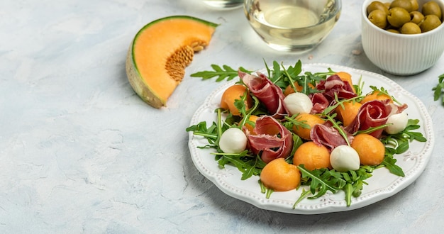Cantaloupe melon with prosciutto or jamon mozzarella and green basil leaves traditional Spanish and Italian appetizer served with wholemeal grissini top view